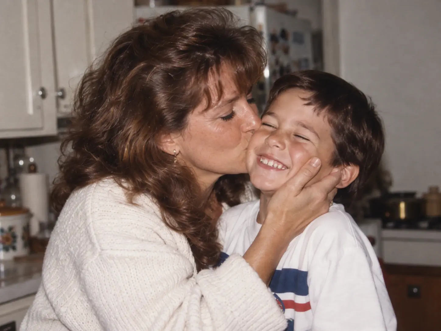 Generated archival-style concept: woman kissing a smiling boy on the cheek in a kitchen.